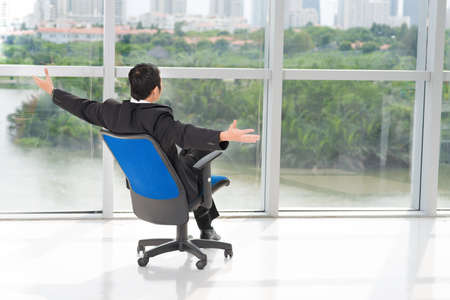 Rear view of a businessman sitting on a chair with opened hands to the natureの写真素材