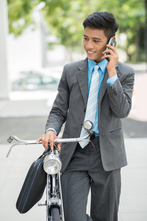 Vertical image of a businessman talking by phone and riding a bicycle on the way at workの写真素材