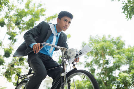 Image of an active modern businessman riding a bicycle viewed below の写真素材