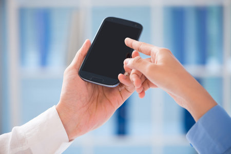 Close-up of a male hand with a smartphone, a female hand pointing at its display