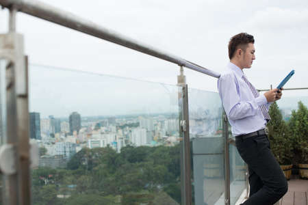 Profile image of a young businessman standing with a gadget during the break outsideの写真素材