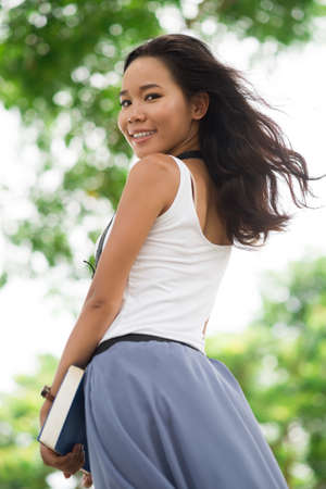 Vertical portrait of a carefree brunette with a book looking over her shoulderの写真素材