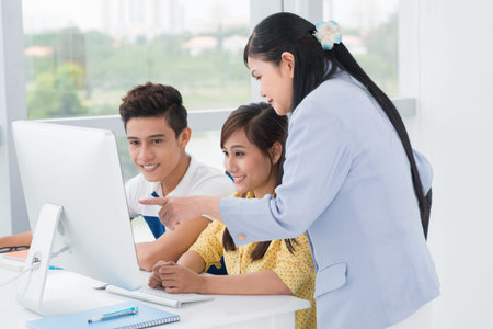 A teacher explaining something to her students pointing at the computer