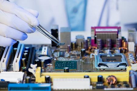 Close-up of a human hand holding tweezers with a computer detail on the foreground