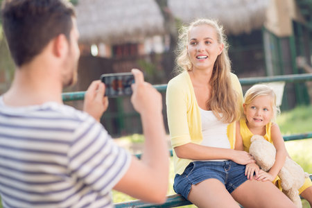 Image of a father making a picture of his wife and daughter in the parkの写真素材