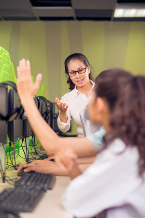 Vertical image of a teacher asking her pupils to answer while one of them putting up his hands on...