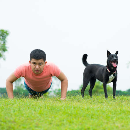 Portrait of a young man doing push-ups with his friend-dog in the parkの写真素材