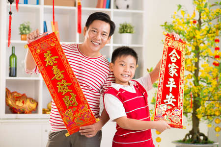 Ñlose up portrait of a father and his son holding red textiles with greetings for the New Year on the foreground の写真素材