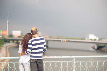 Back view of a young couple standing and bonding on the bridgeの写真素材