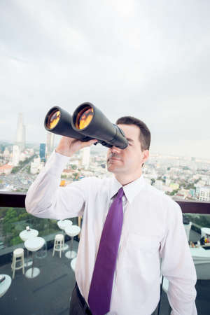 Vertical image of a businessman with the binoculars standing on the roofの写真素材