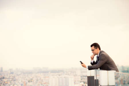 Copy-spaced image of a serious businessman standing on the roof and holding a mobile phone の写真素材