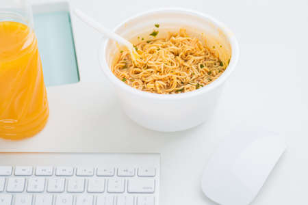 Bowl of instant noodles standing near keyboard and computer mouse on the office deskの写真素材