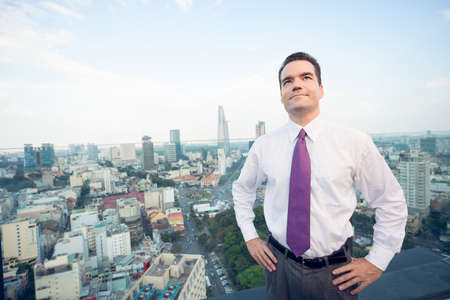 Copy-spaced image of a smiley businessman standing on the roof on the building の写真素材