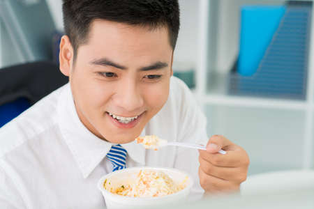 Happy businessman eating chopped vegetables in officeの写真素材