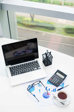 Vertical image of an office desk with a laptop, stationary and financial reportsの写真素材