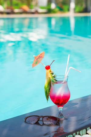 Vertical image of a glass of fresh cocktail with a pineapple slice near the swimming poolの写真素材