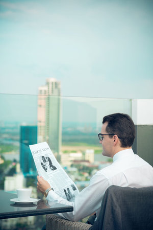 Vertical image of a businessman in eyeglasses reading the newspaper during his coffee breakの写真素材
