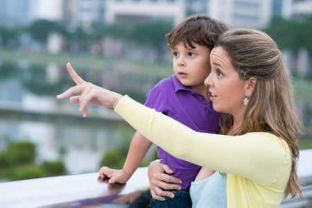 Close up image of a mother holding her son on hands and pointing at something in the streetの写真素材
