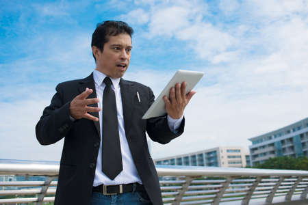 Portrait of a shocked asian businessman holding touchpadの写真素材