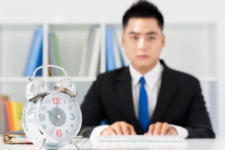 Image of a concerned businessman with an alarm clock in the foregroundの写真素材