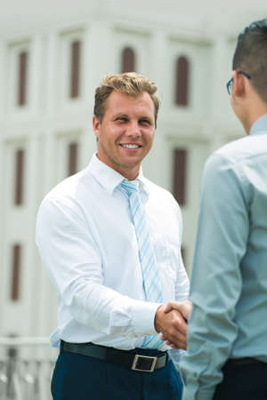 Vertical image of a smiling business guy giving a welcoming handshake to his partner の写真素材