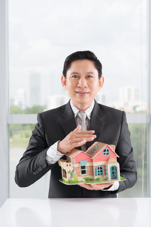 Vertical portrait of a broker showing a house model for saleの写真素材