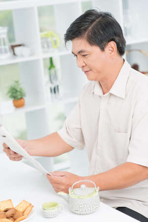 Vertical portrait of a mid-age man spending his morning over tea and a newspaperの写真素材