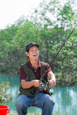 Portrait of a senior excited fisherman catching the fishの写真素材