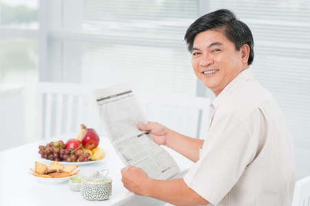 Portrait of a cheerful mid-age man having a snack and a readingの写真素材