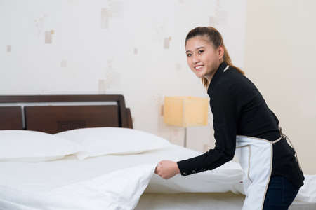 Chamber maid making bed in a hotel roomの写真素材