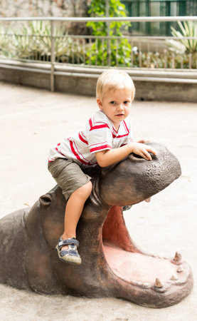 Vertical portrait of a boy sitting on the hippopotamus monument in the zooの写真素材