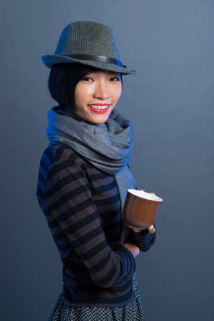Vertical portrait of a young woman in warm clothing with a coffecup in handsの写真素材