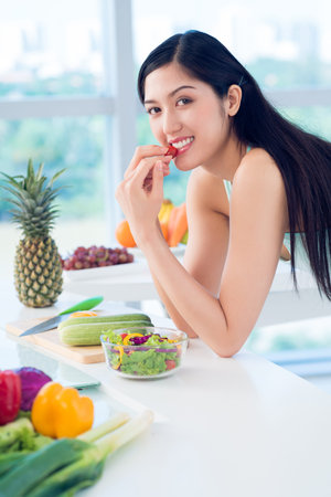 Vertical portrait of a lovely young woman eating fresh fruit and vegetablesの写真素材