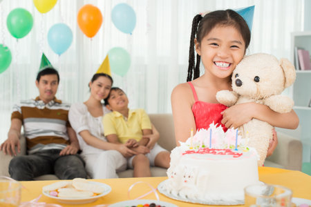 Portrait of a young girl with a teddy bear in hands on her birthday party on the foreground