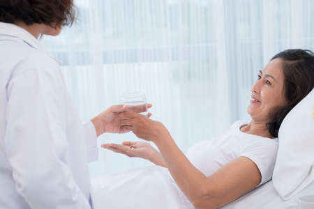 Image of a nurse giving her patient a glass of water to take remedy in the clinicの写真素材