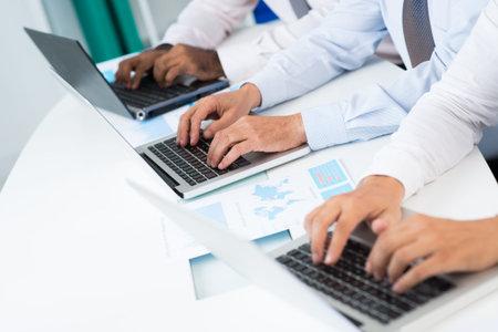 Row of hands businessmen typing on laptops in office