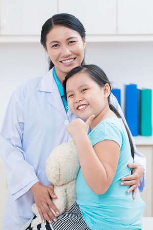 Vertical portrait of a cheerful little patient showing okay posing at camera with a doctor on the foregroundの写真素材