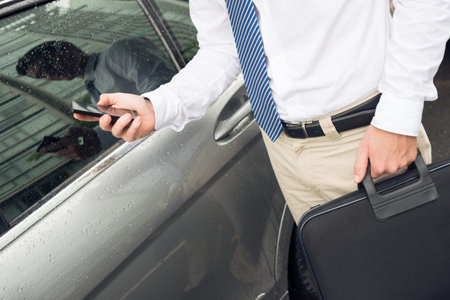 Cropped image of a modern businessman standing with a smartphone near his car outside