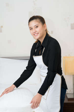 Vertical portrait of a young chambermaid bedding in the apartmentの写真素材