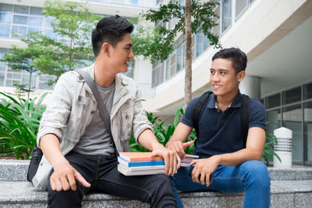 Image of modern young student sitting with books and talking outsideの写真素材