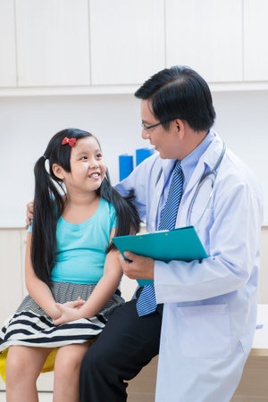 Vertical image of a pediatrician talking with his little patient after examination in the hospitalの写真素材