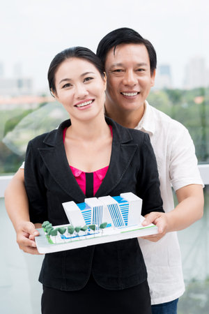 Vertical portrait of a mid-aged couple holding a paper model of their new houseの写真素材