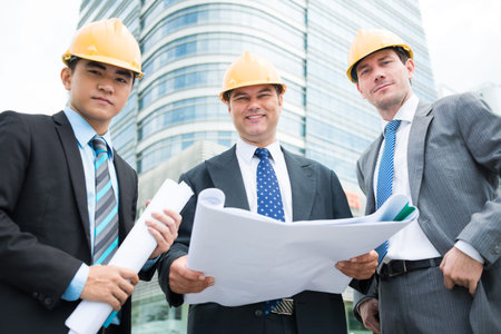 Angle view of constructor workers with drafts in hands smiling and looking at camera
