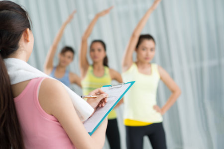 Back view of a trainer making notes while the sportswomen training in the aerobics class