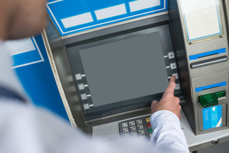 Cropped image of a businessman pressing ATM keyboard to take the money on the foregroundの写真素材