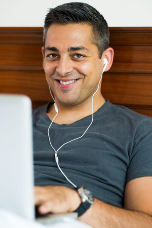 Vertical portrait of a cheerful young man with earphones smiling and looking at camera on the...
