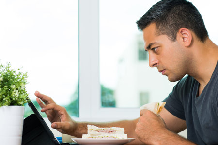 Profile view of a young man having morning breakfast and concentrated at networking at homeの写真素材