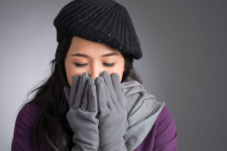 Close-up of a young woman catching a cold over a grey backgroundの写真素材