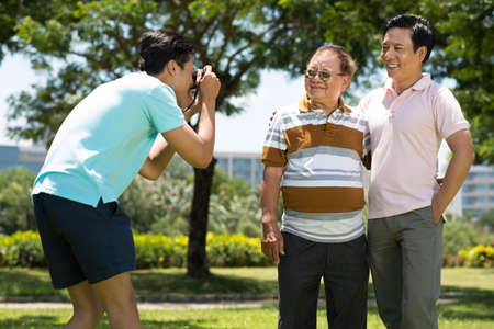 Image of a grandson making a picture of his father and his grandfather in the parkの写真素材
