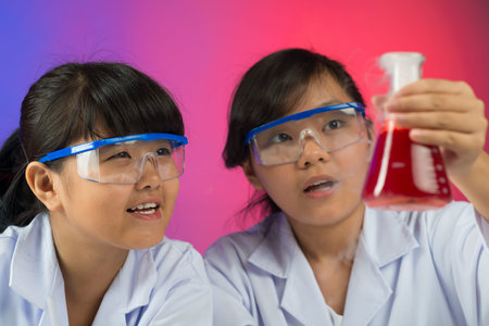 Close-up image of young chemists testing red liquid in the lab